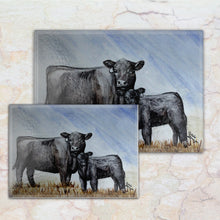 Load image into Gallery viewer, “Tempered glass cutting board featuring a watercolor illustration of a black Angus cow in a grassy pasture – classic farmhouse kitchen decor with rural charm.